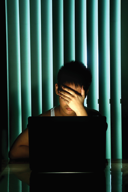 teen in dark room at laptop with hand over face