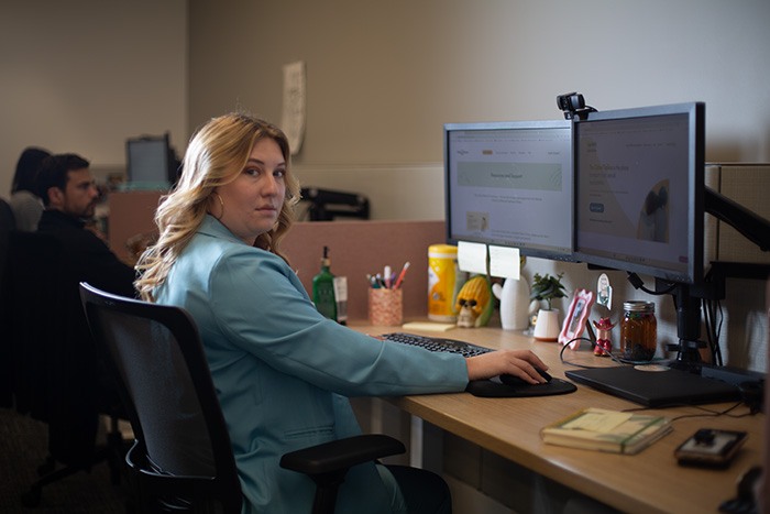 hayley, wearing light blue jacket, works from her desk
