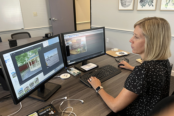 jen sits at a desk in a black top, analyzing multiple photos across two computer screens