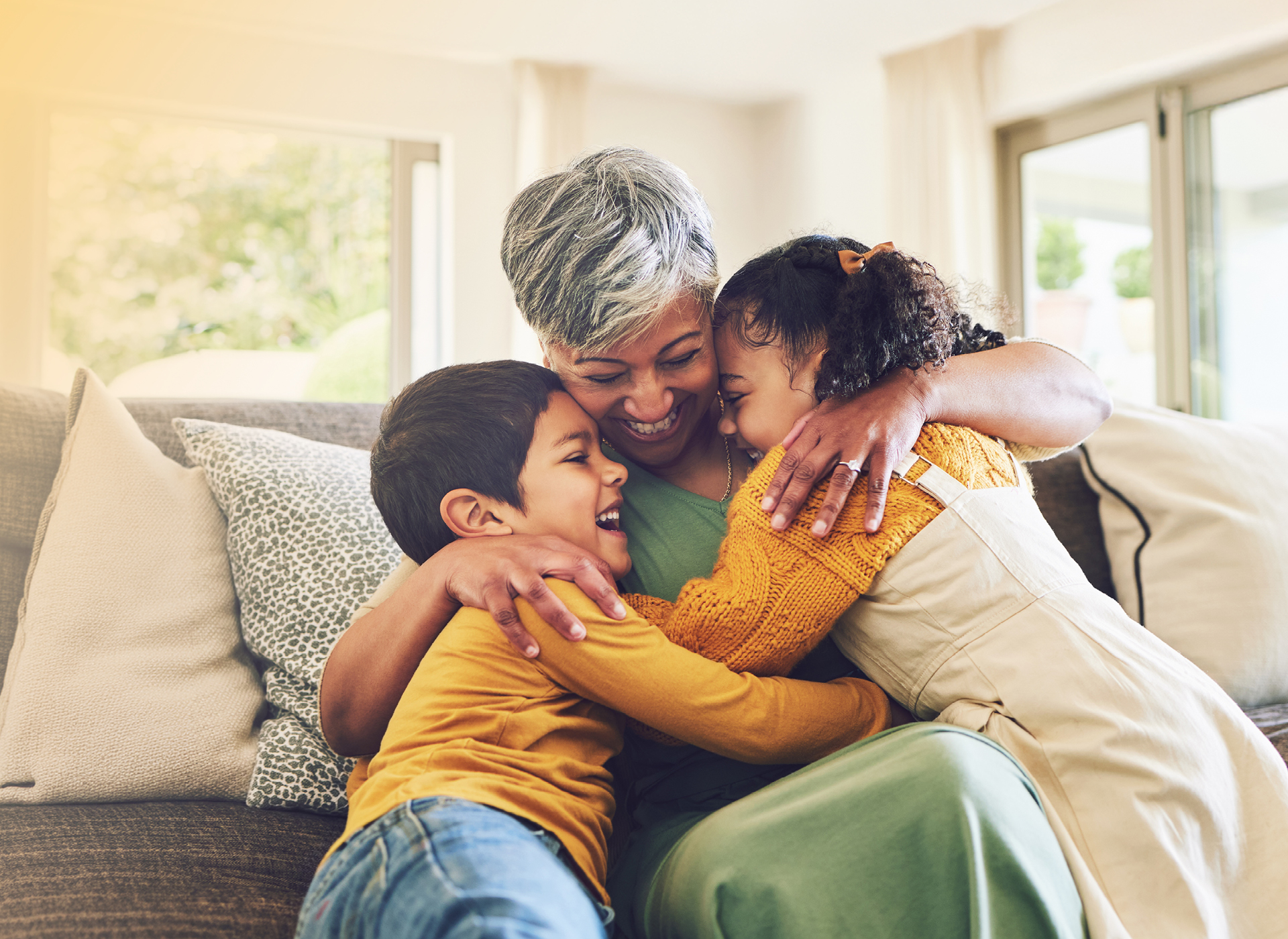 a mom sits on a sofa and hugs two small children