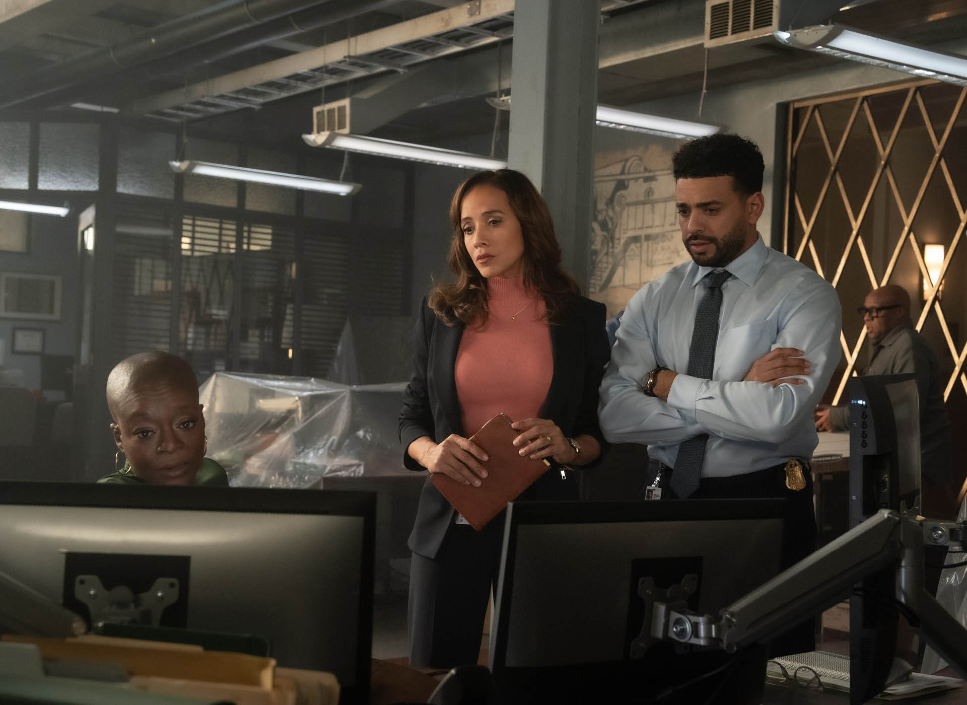 two women and one man look at computers in a police station