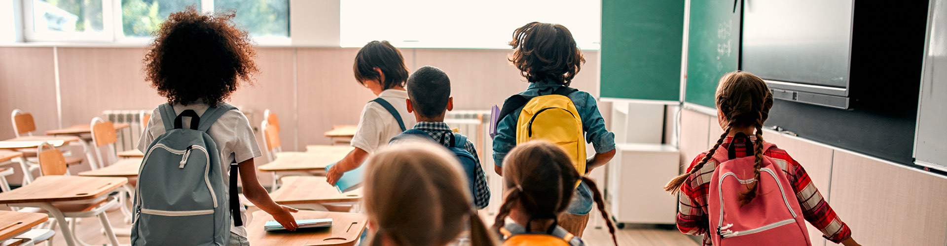 Children walking around a classroom wearing backpacks