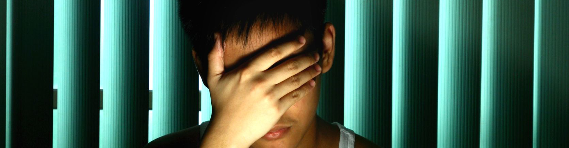 a teenage boy in front of a computer with his hand over his face