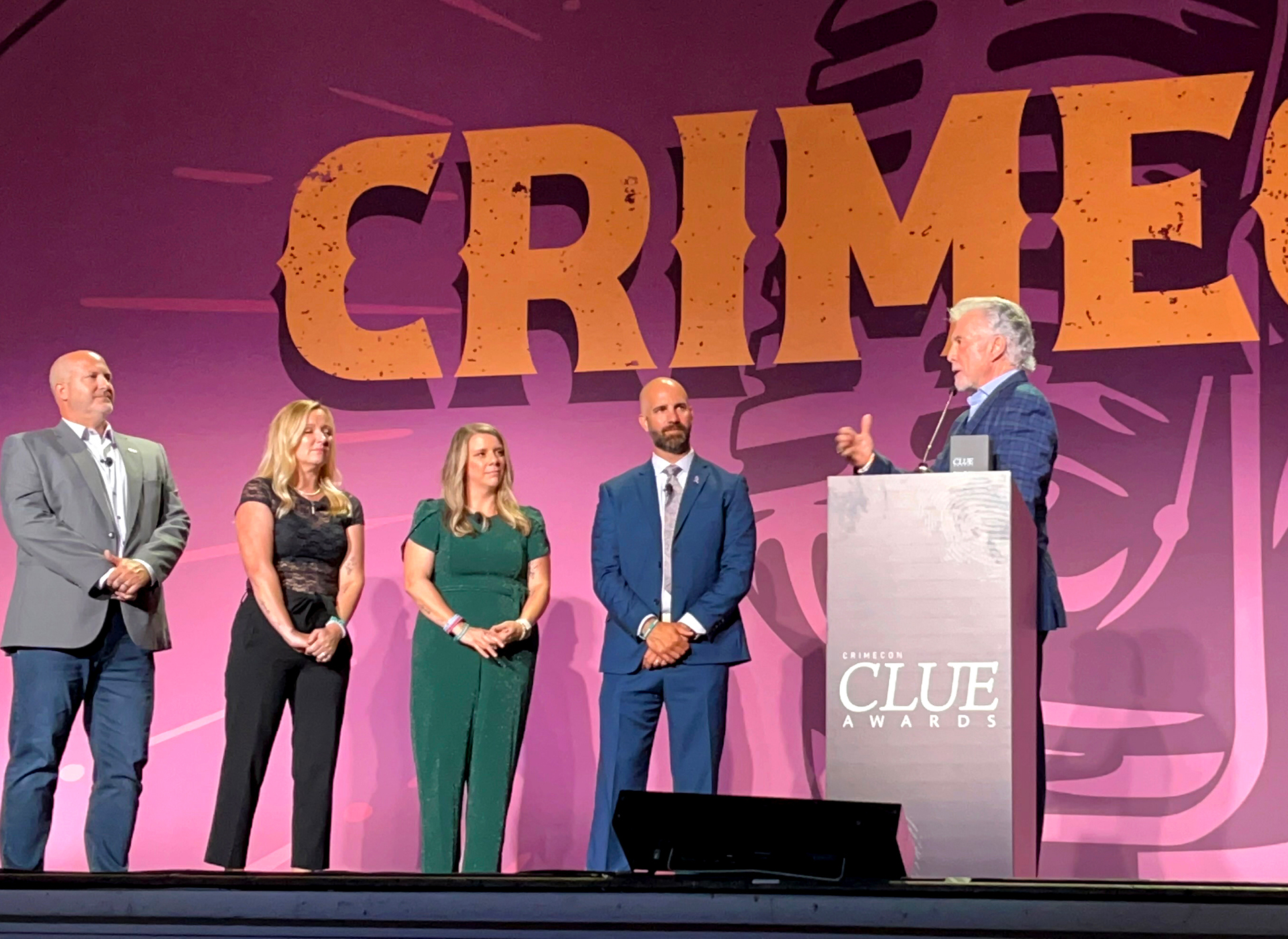 john walsh stands at a podium accepting award next to four members of the gabby petito foundation