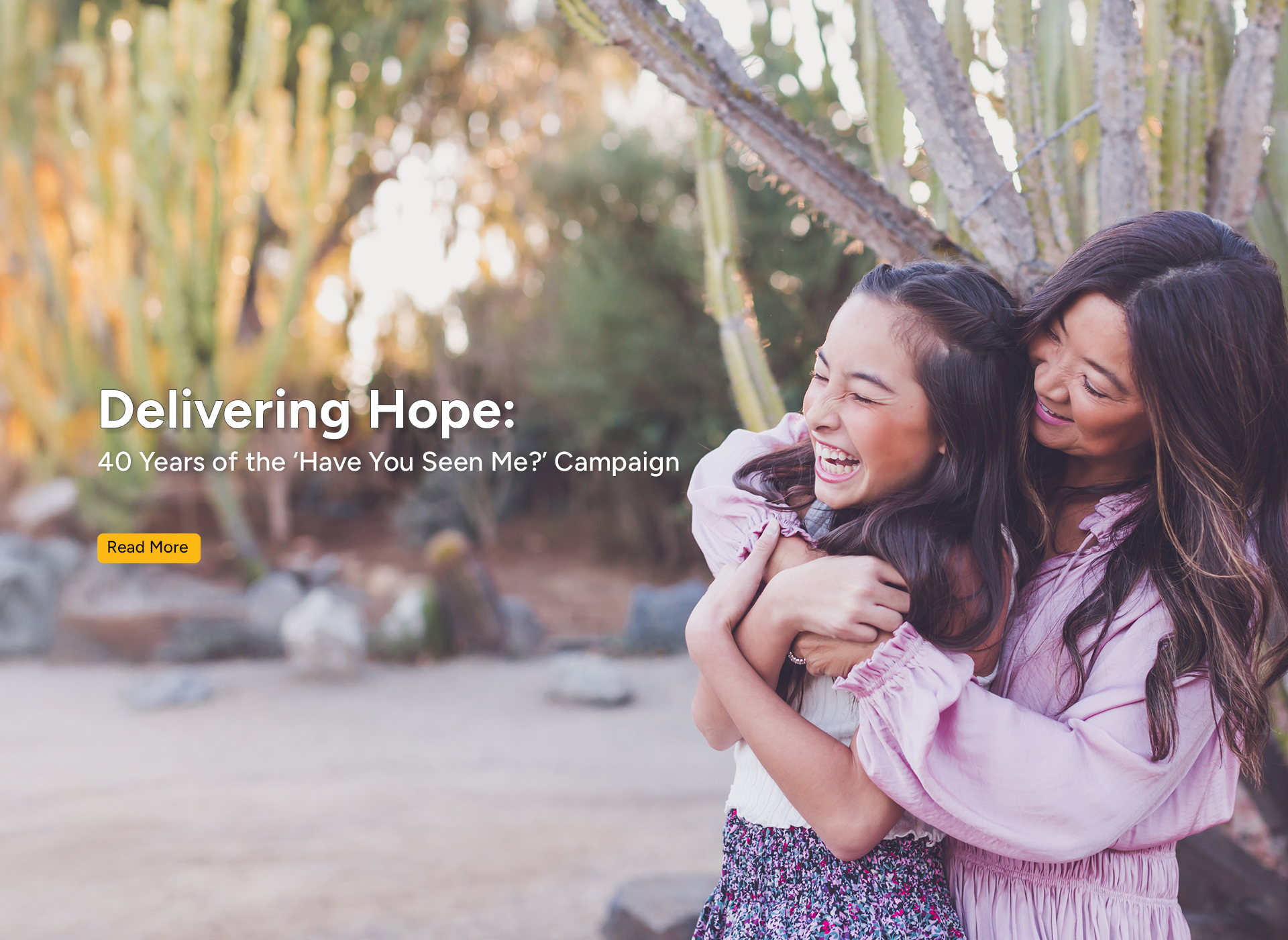 woman and young girl smile and hug by a tree