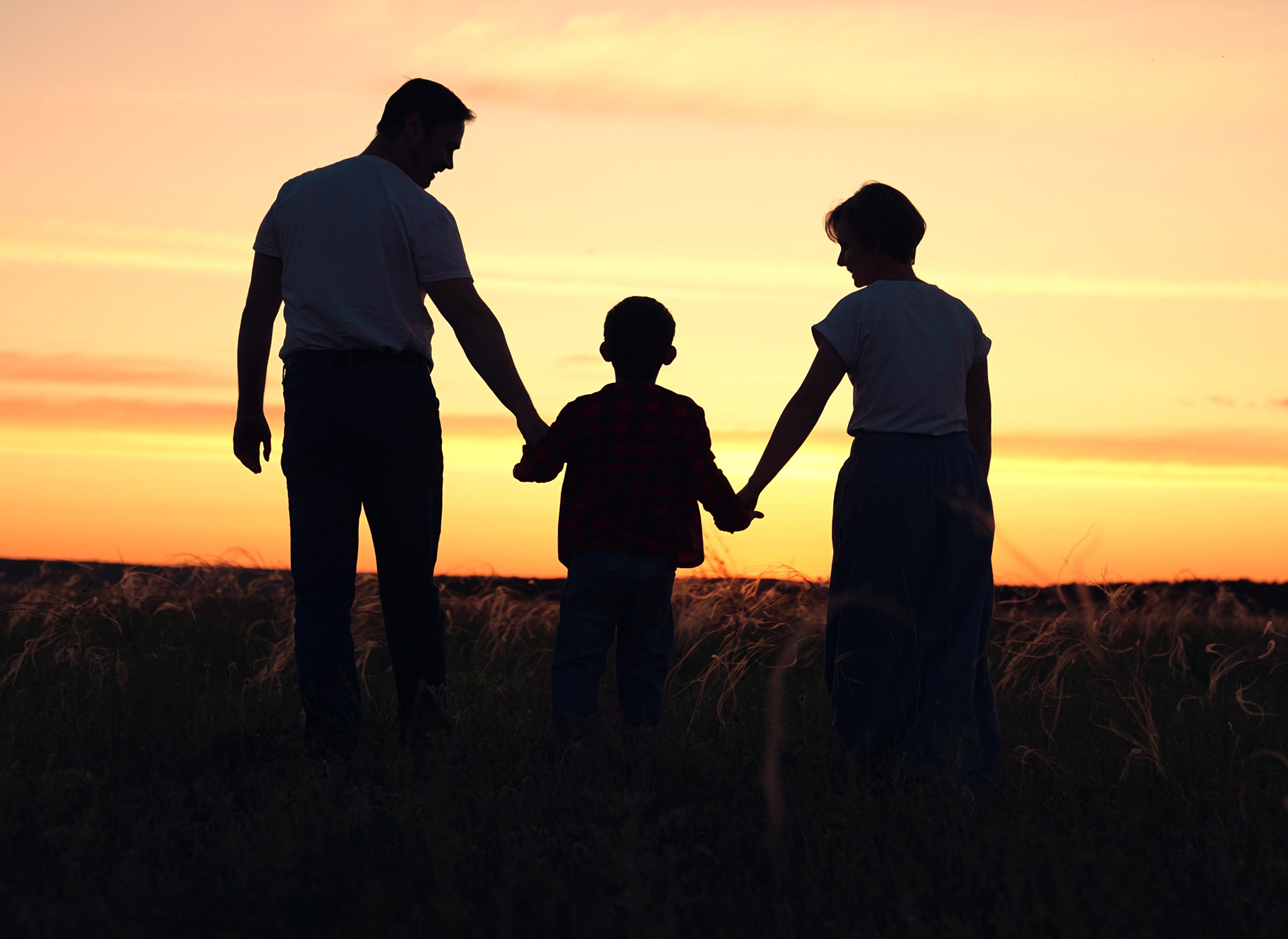silhouette of man and woman holding little boy's hands against the sunset