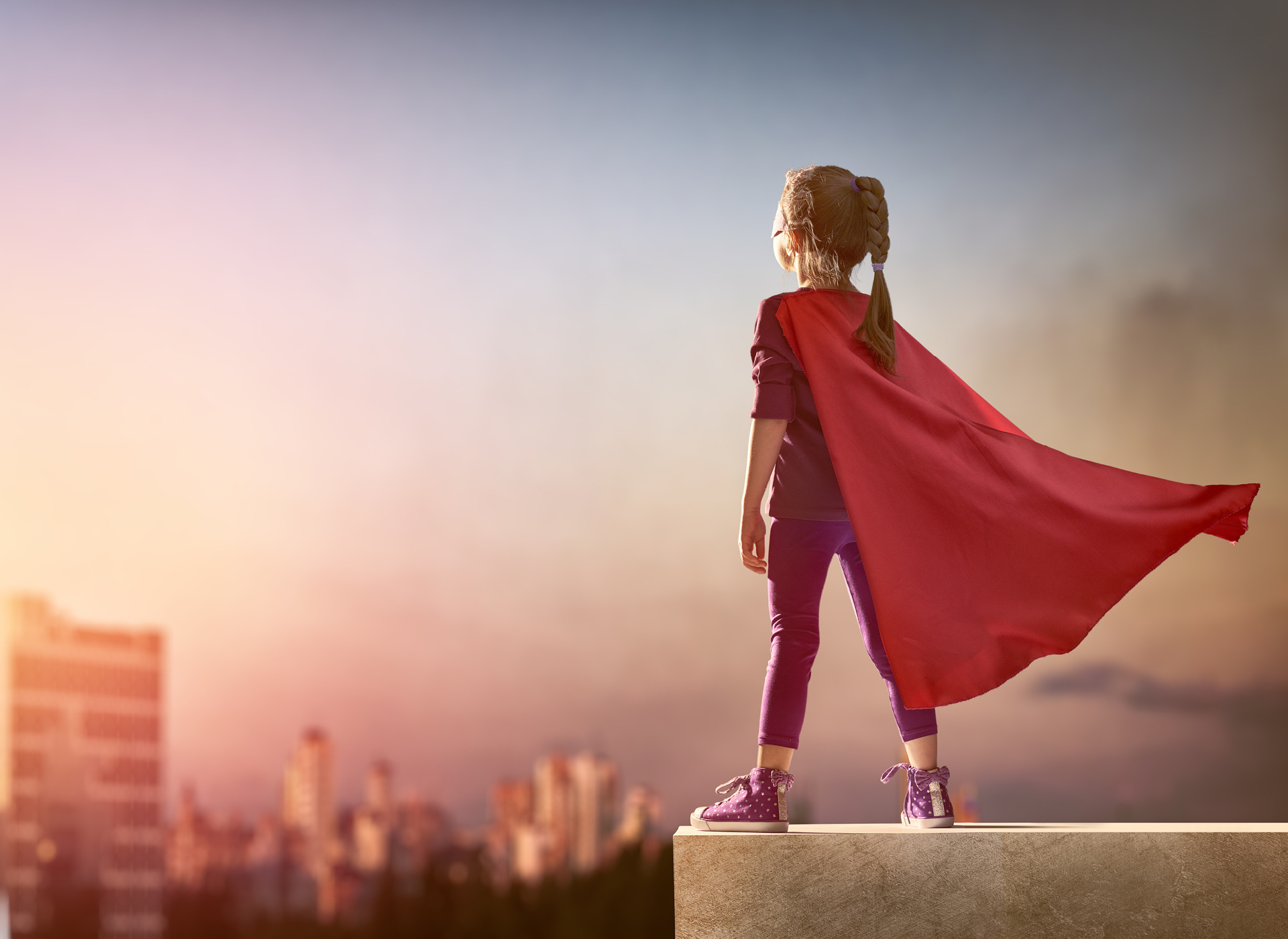 Girl on the edge of a building wearing a superhero cape