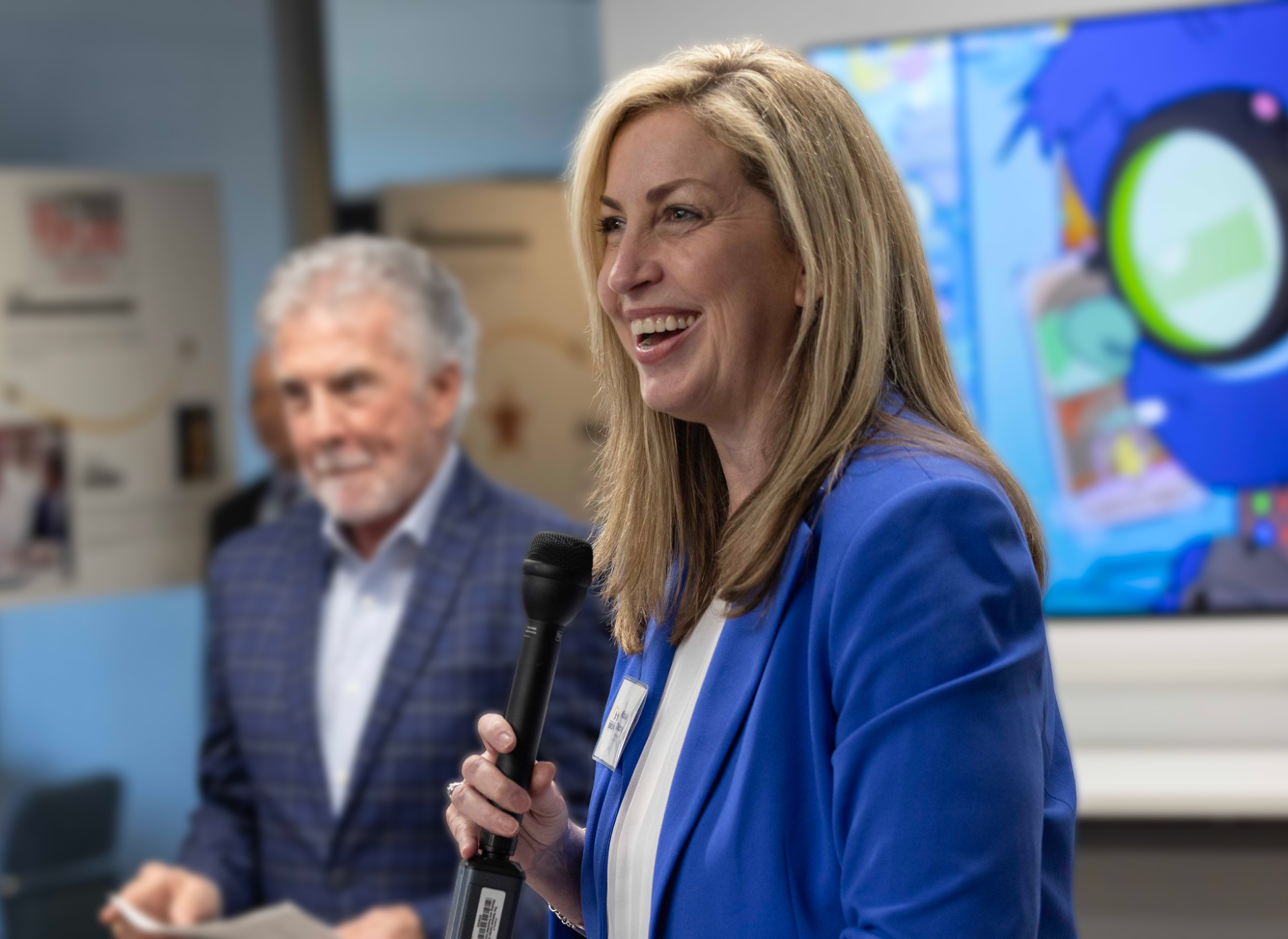 michelle wears blue jacket in foreground, john walsh in dark suit stands in background