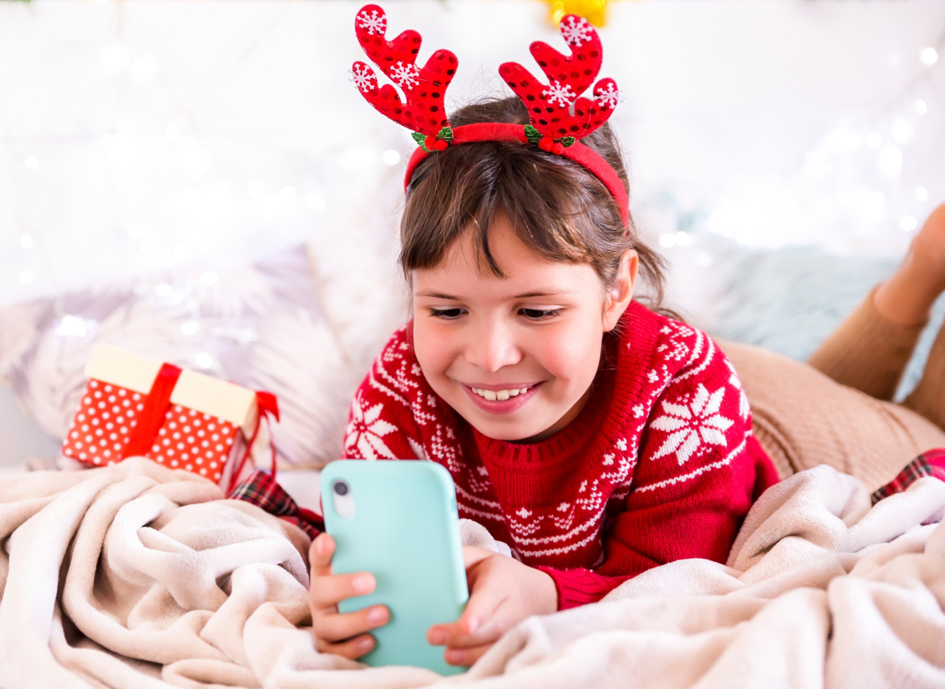 little girl with brown hair and red sweater looking at smartphone smiling