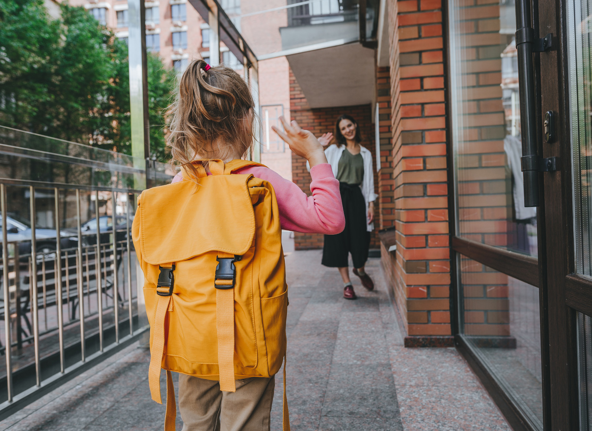 little girl with yellow backpack waving to adult